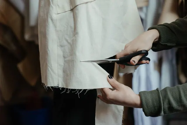 Hands cutting fabric with scissors in a workshop, showcasing the craft of tailoring and fashion design. Putting a real process behind circular fashion design