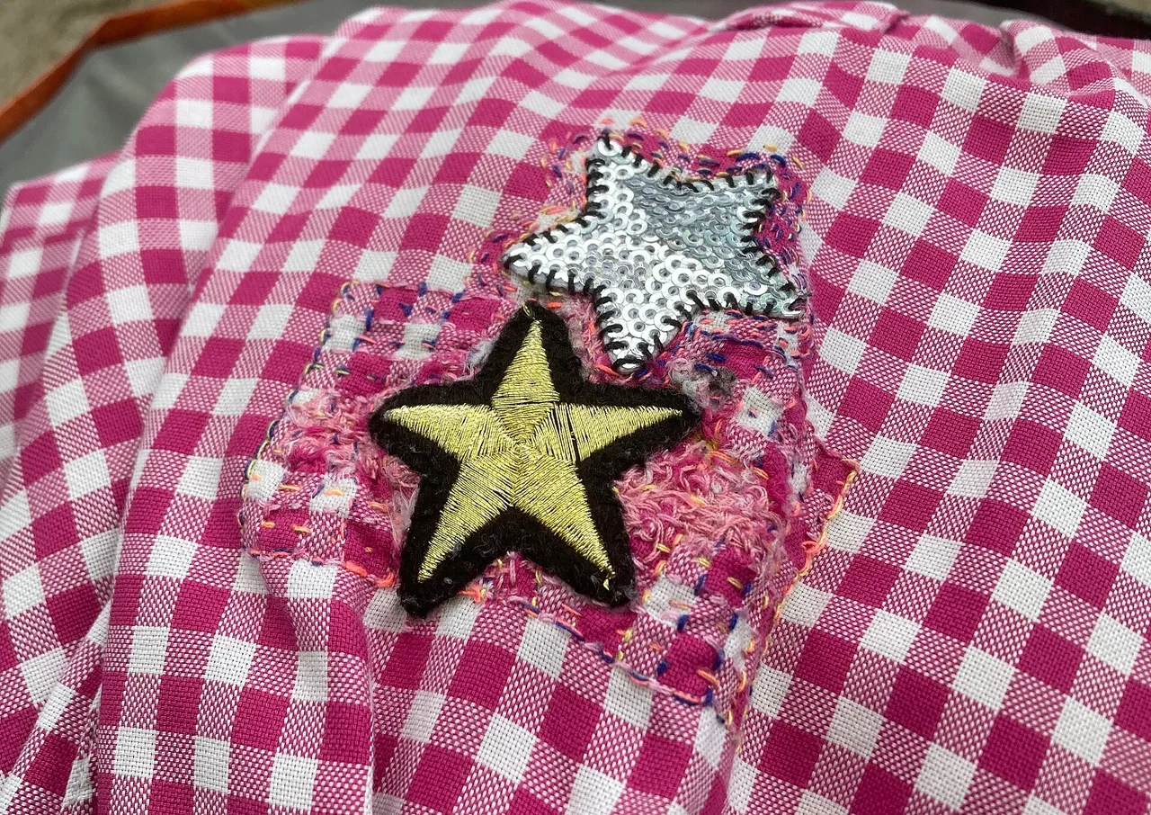 A checked garment repaired with fabric, embroidery, and star patches